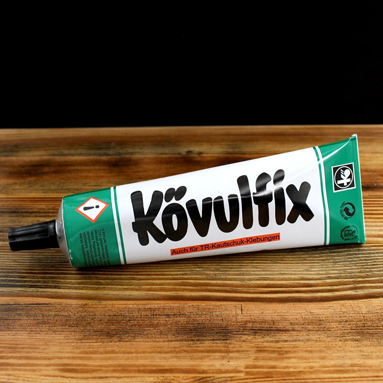Kövultix adhesive tube with green and white design on wooden surface