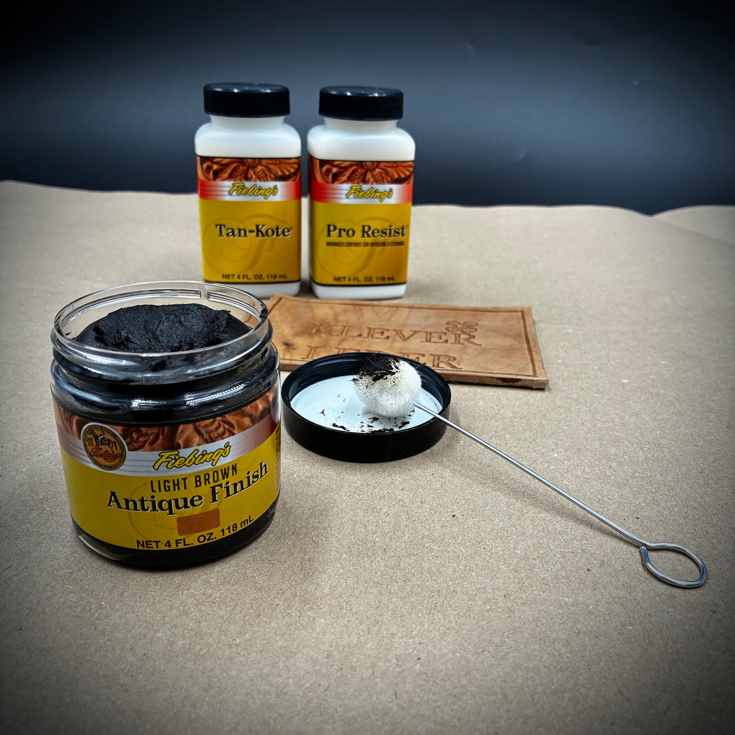 Fiebing's Antique Finish Light Brown und Lederpflegeprodukte auf Basteluntergrund.