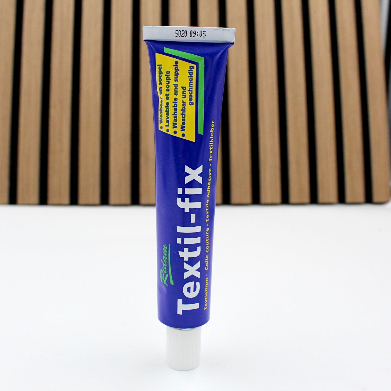 Rote Textilfix Tube Klebstoff für textile und Lederprojekte auf weißem Untergrund vor Holzlatten