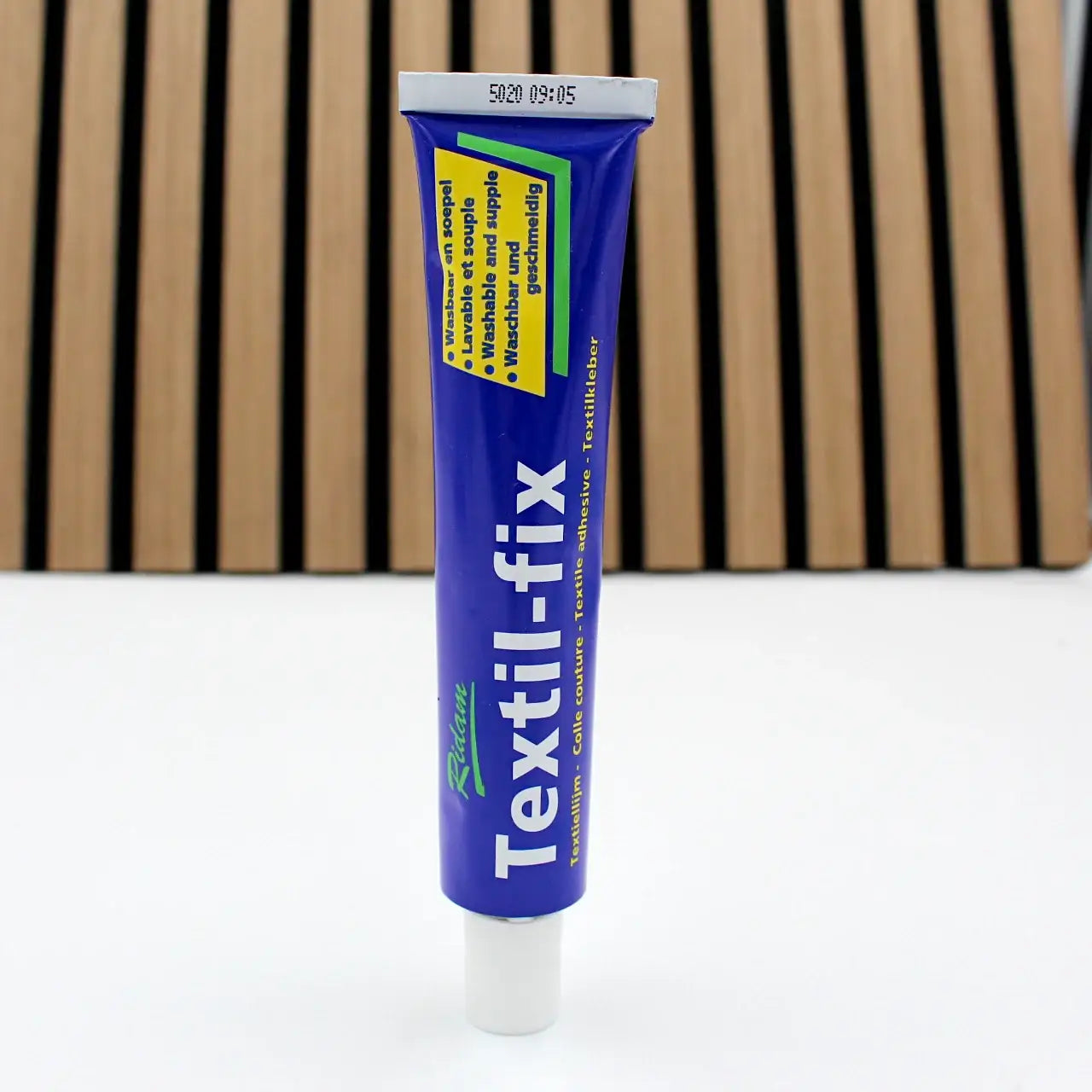 Rote Textilfix Tube Klebstoff für textile und Lederprojekte auf weißem Untergrund vor Holzlatten