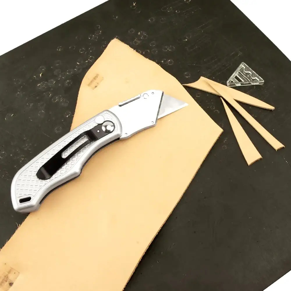 Silbernes Cuttermesser auf hellem Lederstück, Lederreste, Werkzeug für Lederarbeiten