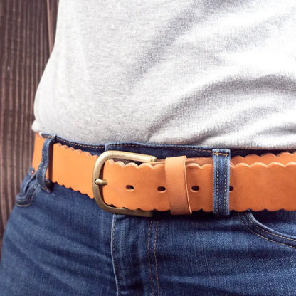 Brauner Ledergürtel mit Zierschnalle und gewelltem Rand an blauer Jeans getragen
