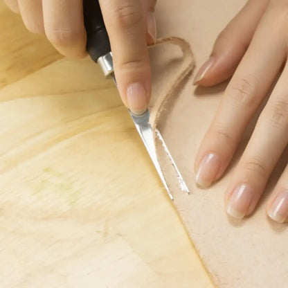 Hand schneidet Naturleder mit Werkzeug auf Holztisch, Lederbearbeitung, Handwerkszubehör