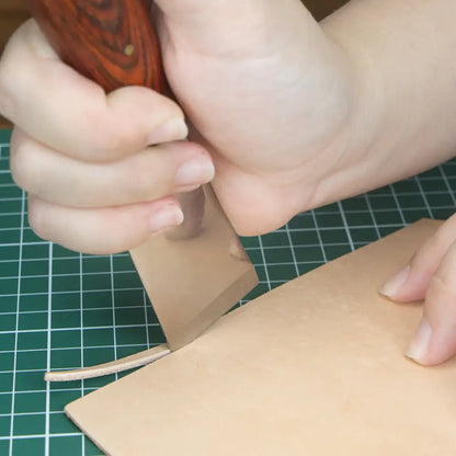 Hand schneidet naturfarbenes Leder mit Messer auf Schneidematte, Lederwerkzeug Detail