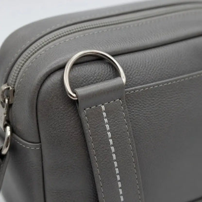 Detail einer grauen Ledertasche mit Metallringen und weißen Ziernähten