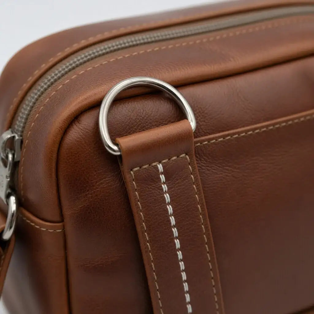 Detailansicht einer braunen Ledertasche mit silbernem Metallring und weißen Nähten
