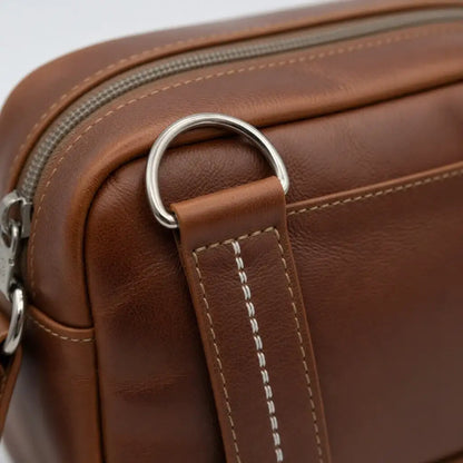 Detailansicht einer braunen Ledertasche mit silbernem Metallring und weißen Nähten
