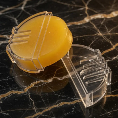 Gelbe Lederpflegecreme in transparenter Halterung auf Marmoroberfläche