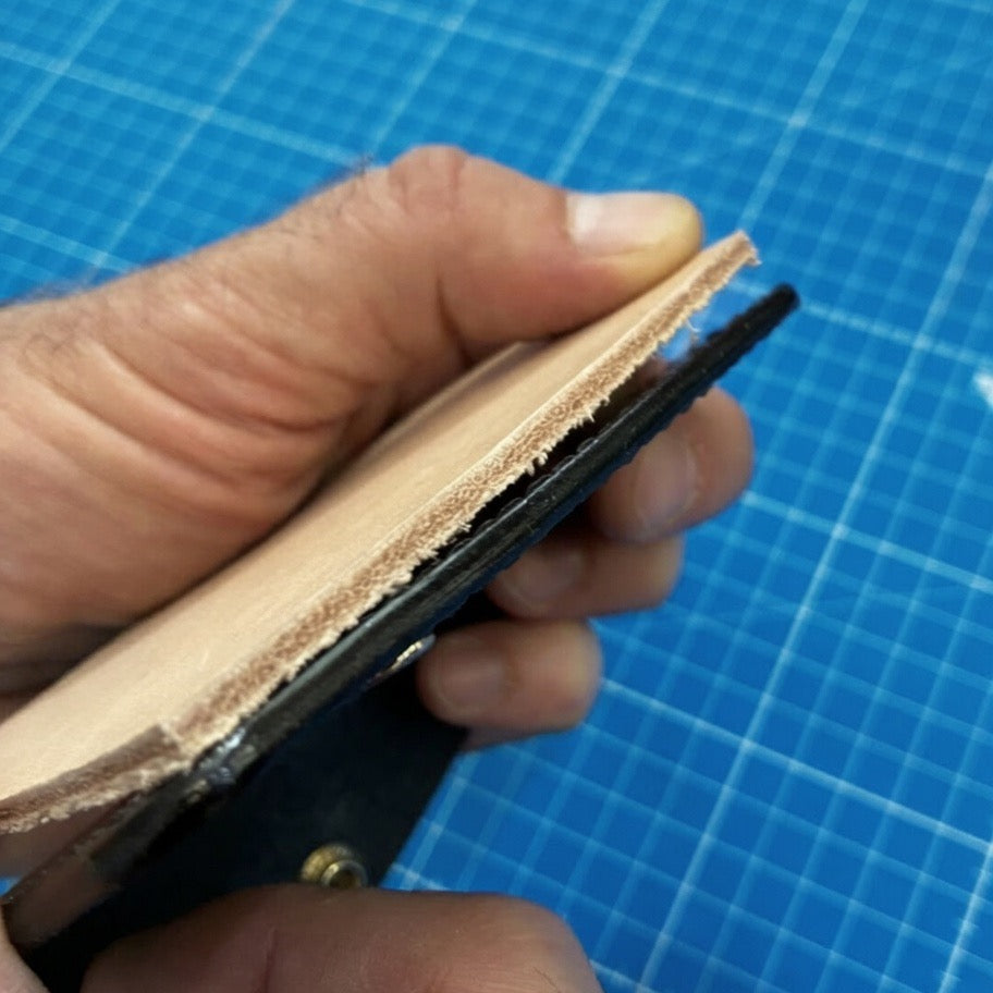 Hand hält Lederstück mit sichtbarer Naht auf blauem Schneidematte