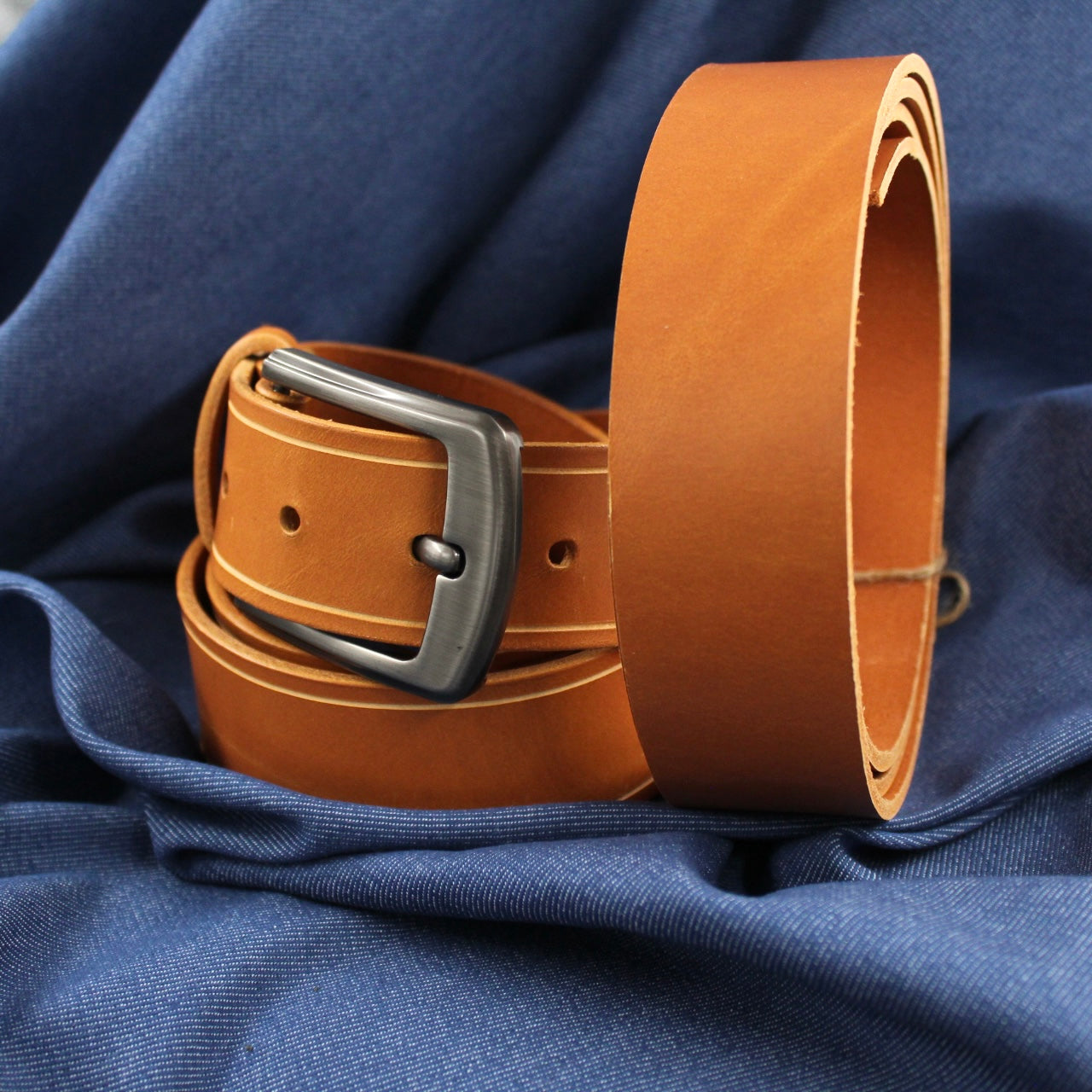 Hochwertiger Lederriemen aus pflanzlich gegerbtem Rindvollleder in Cognac-Farbe, elegant auf dunkelblauem Jeansstoff präsentiert.