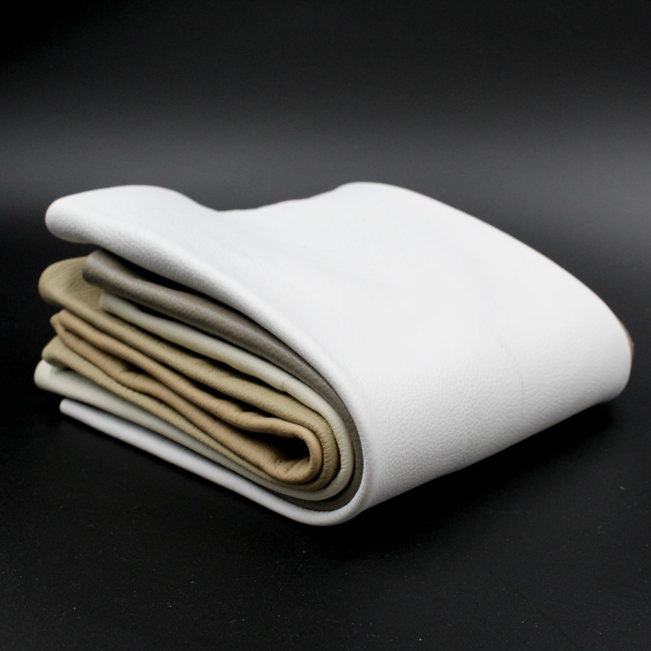 Gefaltete Lederstücke in Weiß und verschiedenen Braun- und Beigetönen auf schwarzem Hintergrund, hochwertiges Material