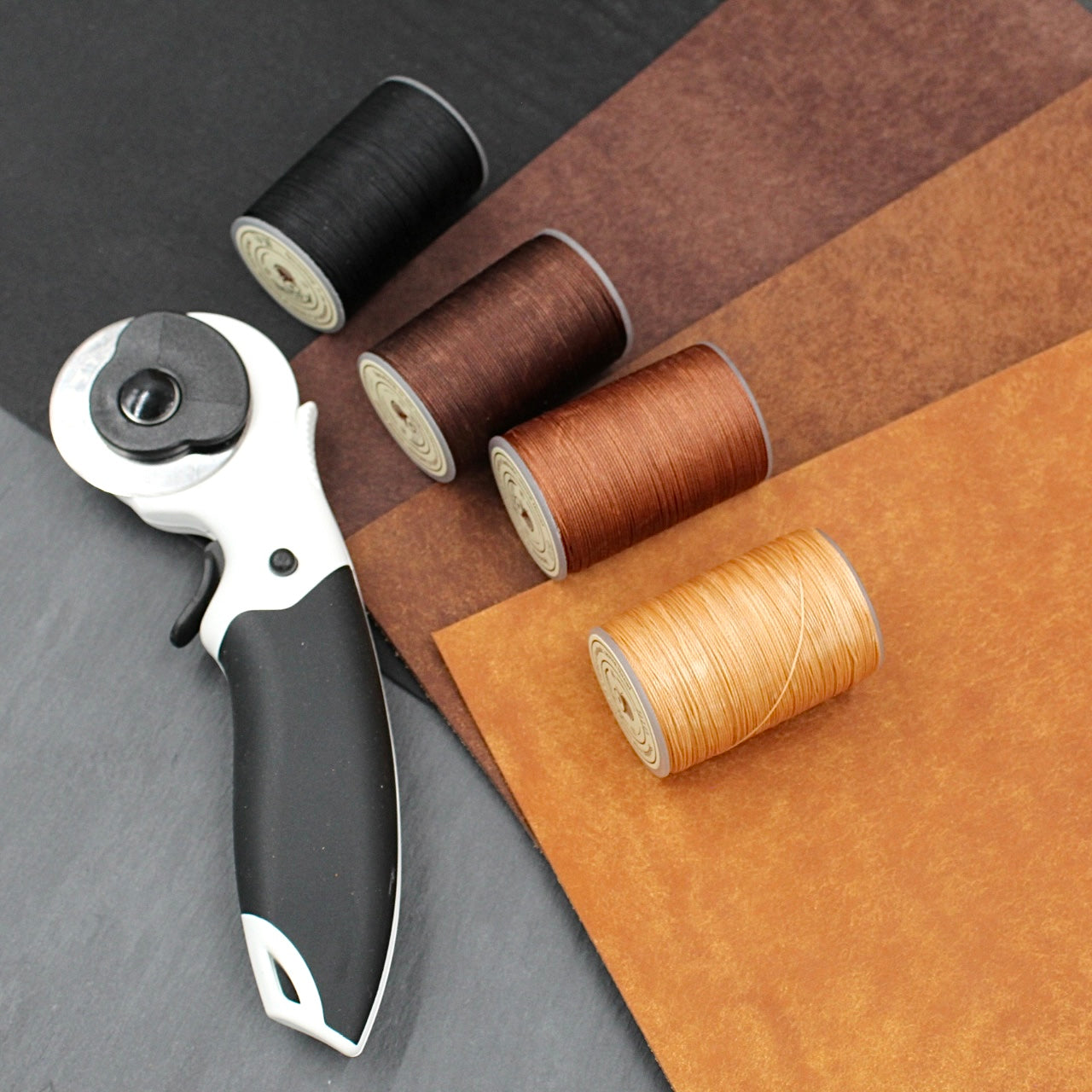 Rollschneider und bunte Nähgarne für Lederprojekte auf dunkler Oberfläche