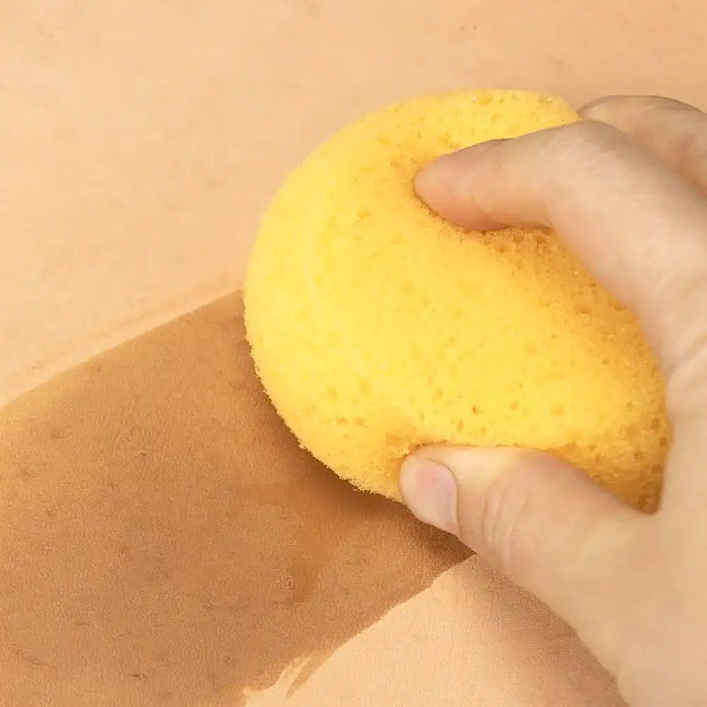 Hand reinigt helles Leder mit gelbem Schwamm, Lederpflege und Lederreinigung