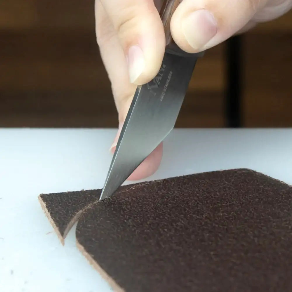 Hand schneidet braunes Leder mit scharfem Messer auf Schneidunterlage