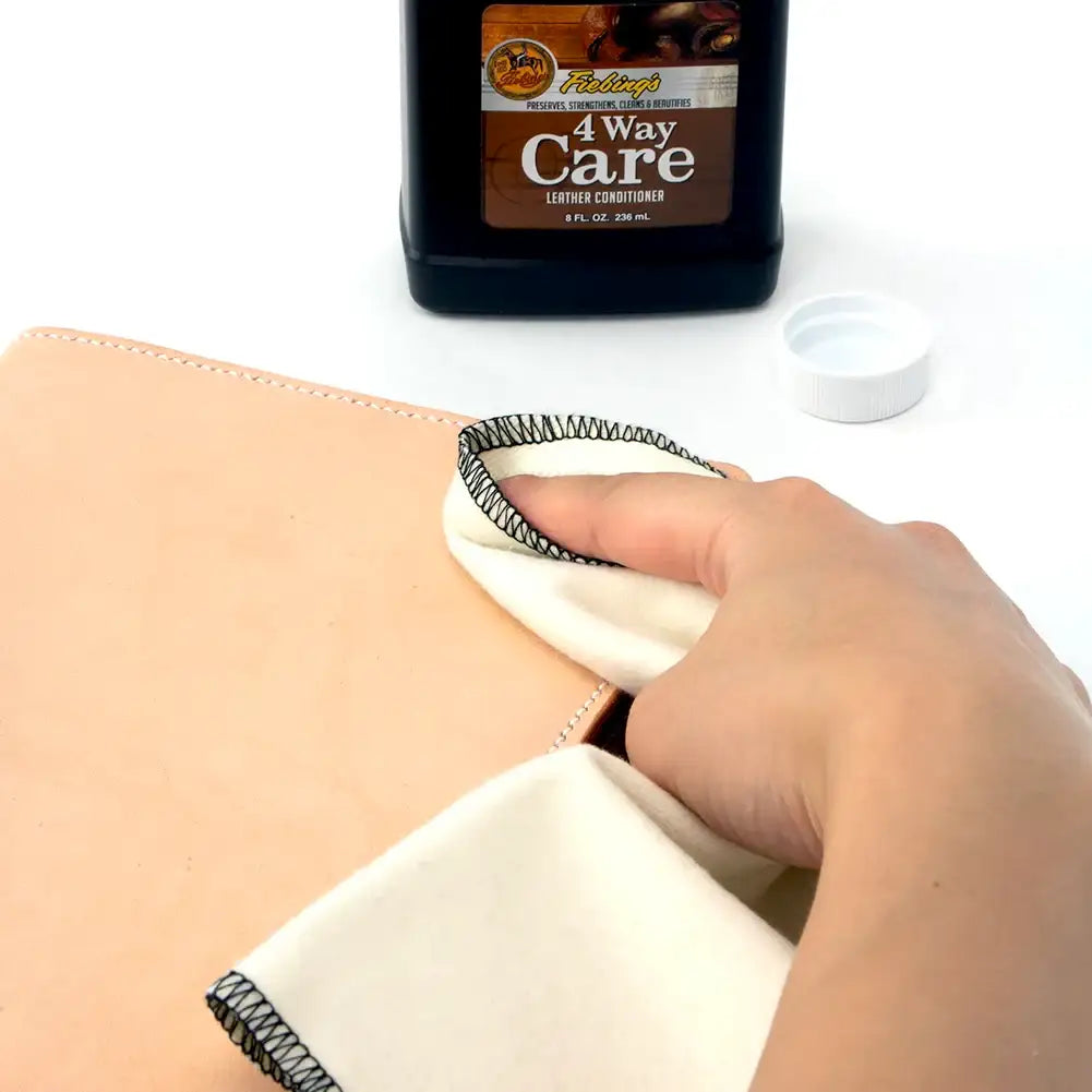 Hand pflegt helles Leder mit Tuch und Lederpflege, Flasche im Hintergrund