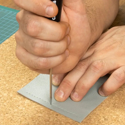 Handwerk mit Leder: Präzise Bearbeitung mit Werkzeug auf grauem Lederstück