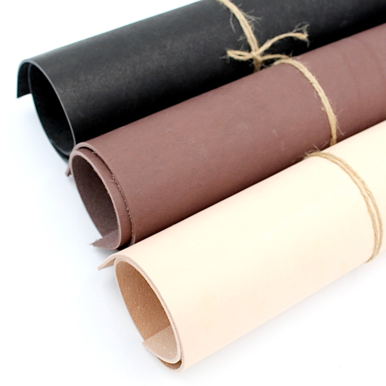 Drei gerollte Lederstücke in Schwarz, Braun und Beige auf weißem Hintergrund, Bastelmaterial