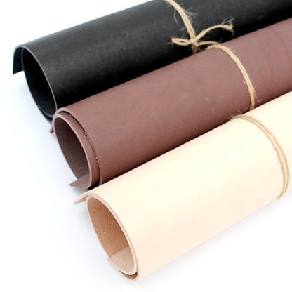 Drei gerollte Lederstücke in Schwarz, Braun und Beige auf weißem Hintergrund, Bastelmaterial