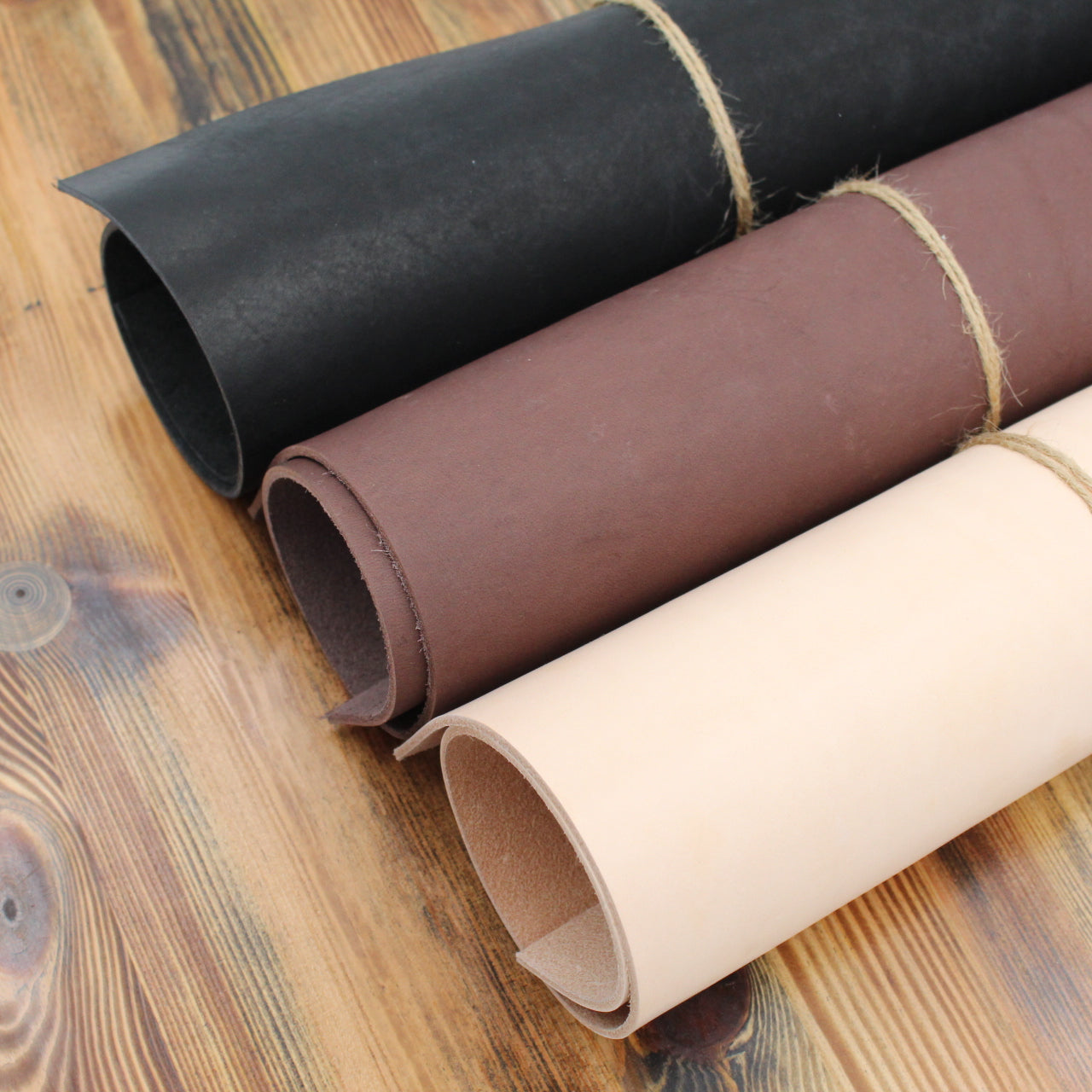 Drei Lederrollen in Schwarz, Braun und Natur auf Holztisch, hochwertiges Leder für DIY-Projekte